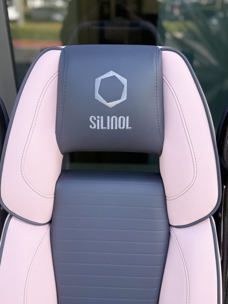 Close up of a marine boat seat headrest with the Silinol logo embroidered in white on navy leather, flanked by blush pink bolsters with navy piping.